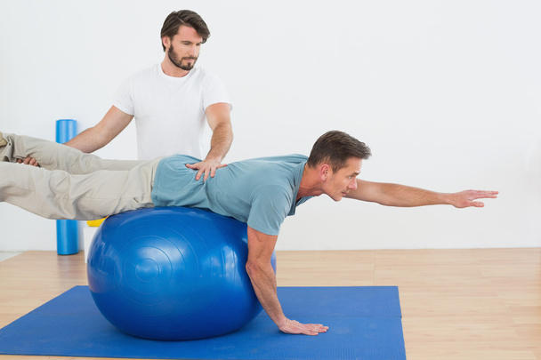 Фізіотерапевт допомагає молодому чоловікові з м'ячем йоги
 - Фото, зображення