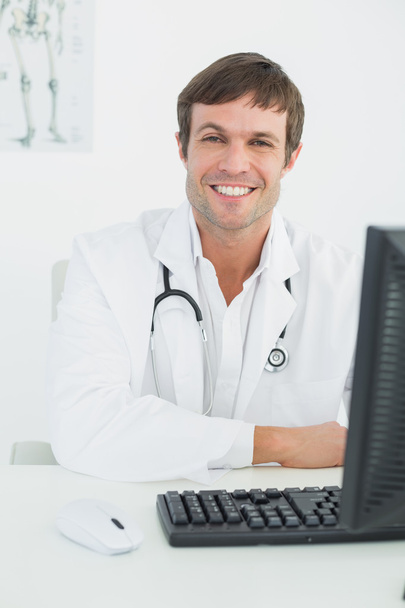Smiling male doctor with computer at medical office - Fotó, kép