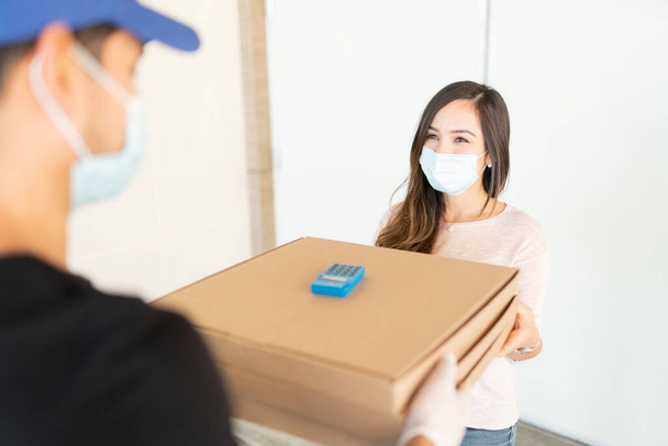 コロナウイルス危機の間に配達人から小包を受け取るミッド大人の女性 - 写真・画像
