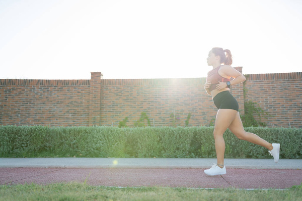 Вид на атлетическую молодую женщину, бегающую в общественном парке против яркого неба - Фото, изображение