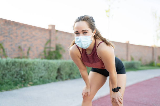 Portrait de jeune femme se reposant après avoir fait du jogging dans le parc pendant la crise du coronavirus - Photo, image