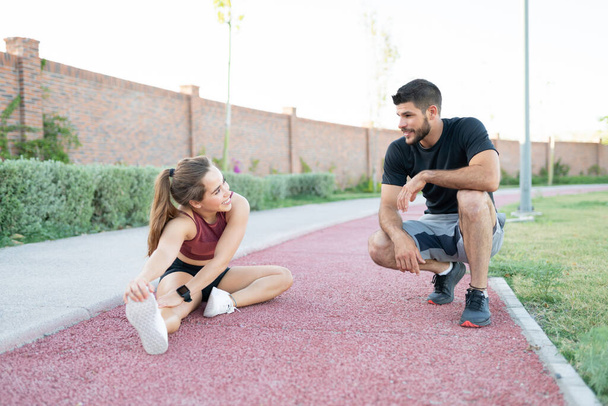 Usmívající se atletický muž a žena mluví při cvičení v parku - Fotografie, Obrázek