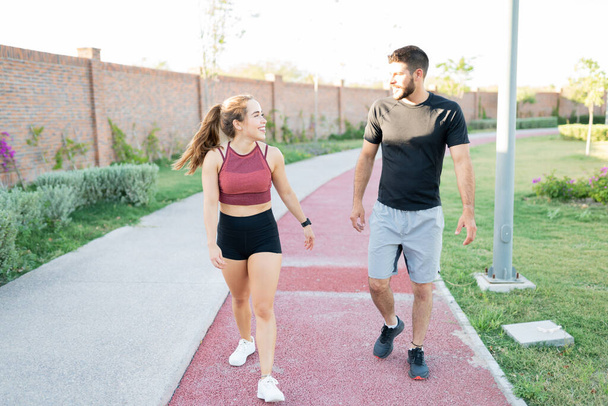Gülümseyen genç adam ve kadın parkta yürürken konuşuyor. - Fotoğraf, Görsel