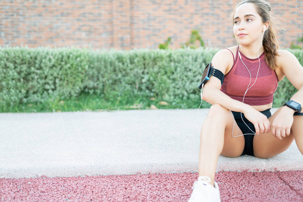 Exhausted athletic young woman taking break while working out in park - Photo, Image