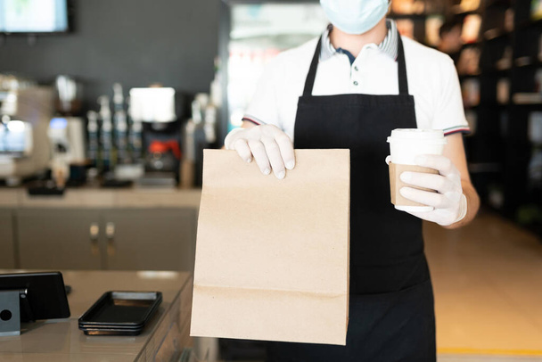 Środkowa część męskiego personelu trzymającego paczkę i kubek jednorazowej kawy przy kawie na wynos w kawiarni - Zdjęcie, obraz