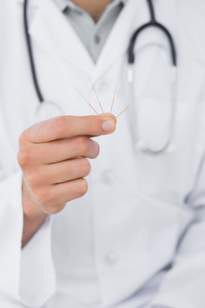 Mid section of a male doctor holding acupuncture needles - Fotó, kép