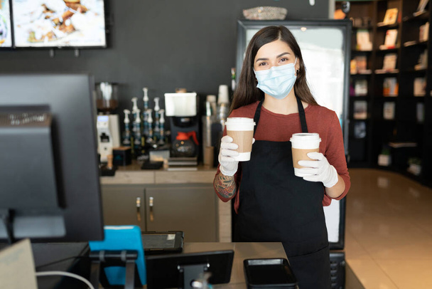 Mitarbeiterinnen tragen Mundschutz und Handschuhe, während sie Kaffee im Café servieren - Foto, Bild