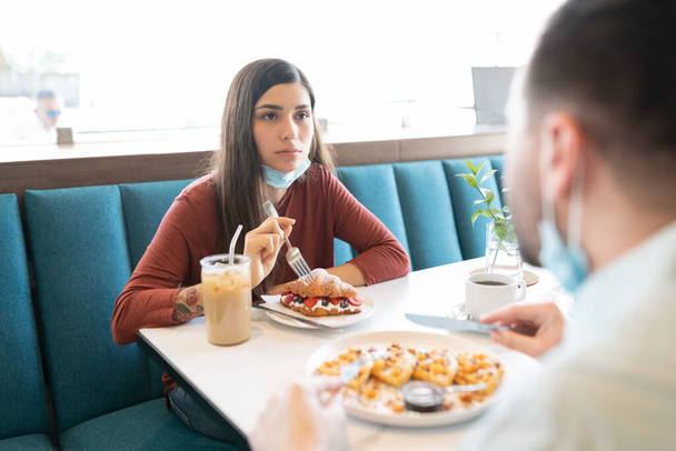 Latin young woman having dessert with man in cafe during coronavirus crisis - 写真・画像