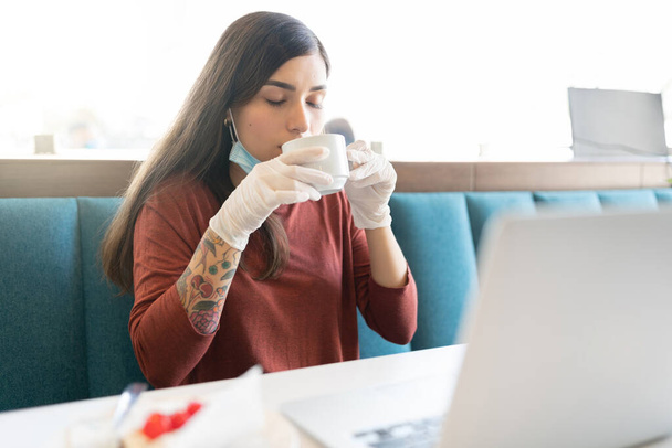 ラテン系の若い女性がコロナウイルス発生中にカフェでコーヒーを飲む - 写真・画像
