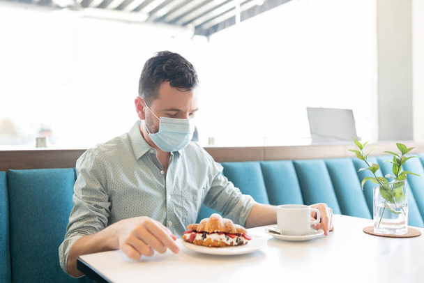 Valkoihoinen mies ottaa makeaa ruokaa ja kahvia ravintolassa aikana coronavirus puhkeaminen - Valokuva, kuva