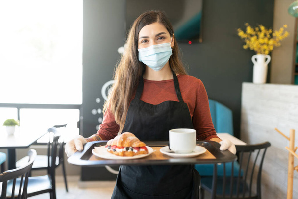 Retrato de camarera con mascarilla mientras sirve el pedido en la cafetería
 - Foto, imagen