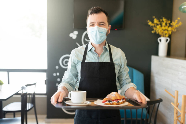 Muotokuva tarjoilija yllään kasvonaamio tarjoillessaan järjestyksessä kahvilassa - Valokuva, kuva