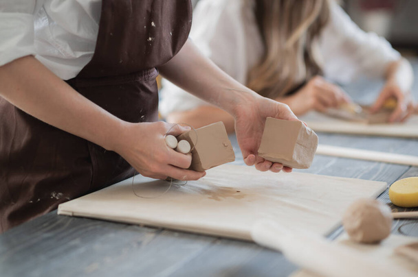White clay preparation for work. Cutting layers of clay pieces for sculpting in the workshop of a potter Close-up. Raw bar of clay on the old wooden table in pottery. - Foto, Imagen