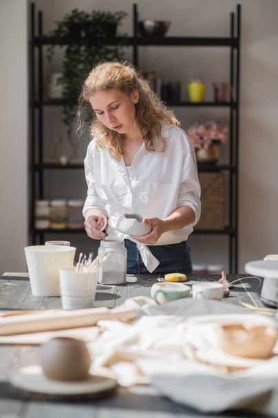Female potter glazing raw unburned ceramic cup using brush. Earthenware mug putting colorant on pottery workshop. - Photo, Image