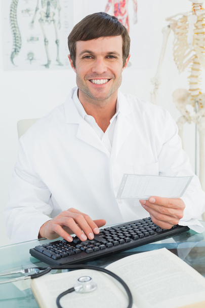Porträt eines männlichen Arztes beim Lesen einer Notiz am Schreibtisch - Foto, Bild