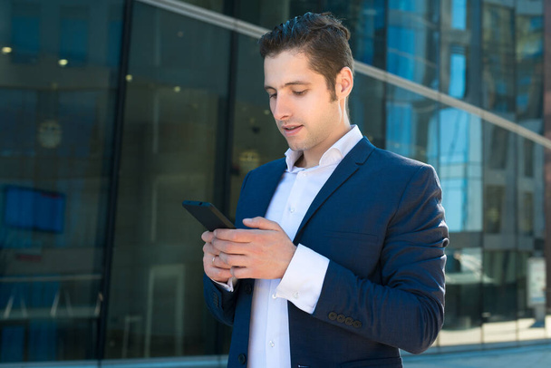 Młody biznesmen w garniturze SMS-a przez telefon  - Zdjęcie, obraz