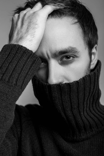 Closeup sexy handsome man wearing warm pullover with high collar and touching hair, looking seductive, flirting at camera, male fashion, vogue concept. black and white, indoor studio shot isolated - Фото, зображення