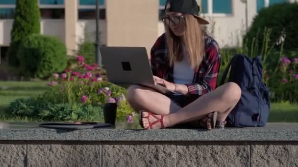 Vysokoškolák pracující na laptopu v kampusu. Krásná mladá studentka sedí v blízkosti univerzity a pomocí přenosného počítače. - Záběry, video