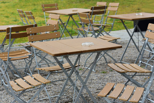 雨の後やドイツのゲストなしで外のレストランの空の木製のテーブルや椅子のシーン - 写真・画像
