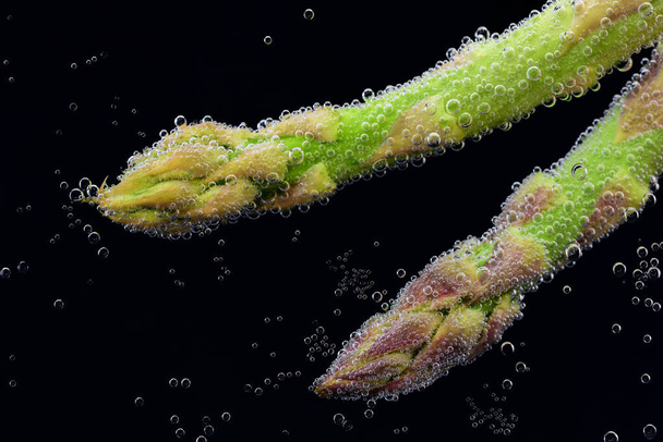 新鮮な緑のアスパラガスは、上方に上昇気泡と黒の背景に水の下の鍋で調理します。 - 写真・画像