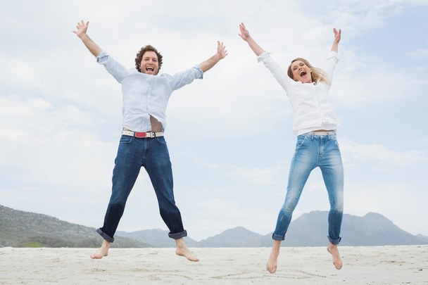 Cheerful young couple jumping at beach - Valokuva, kuva
