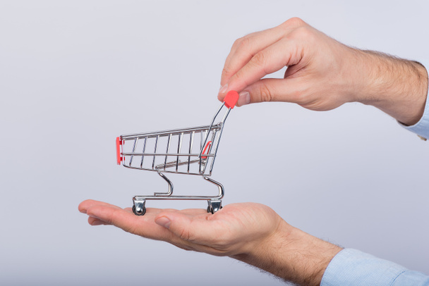 Male hands holding small shopping cart on white background. Side view. - Φωτογραφία, εικόνα