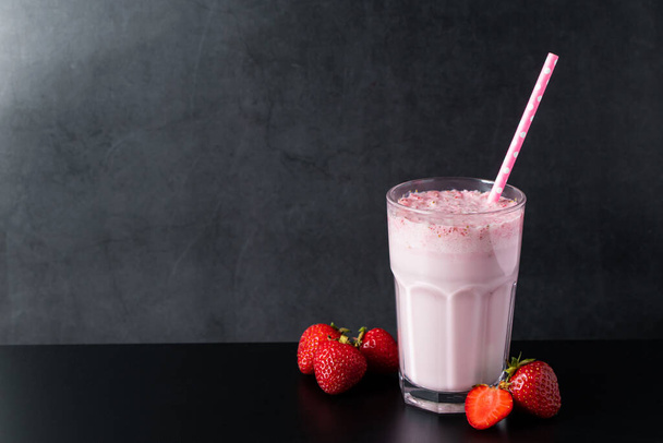 Fresh milkshake with strawberries on a black background. Summer drink with a straw in a glass. Place for text. - Photo, Image