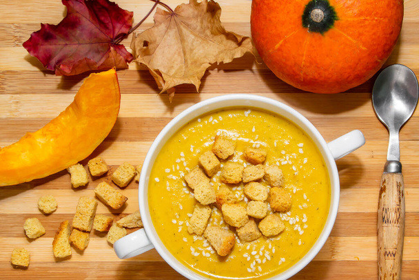 Осенний тыквенный суп с кунжутом на деревянном фоне. Осенняя тыква блюдо - суп с крекерами и кунжутом семена крупным планом вид сверху
 - Фото, изображение