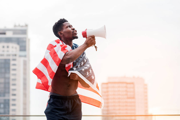 african american man with usa flag shouting into a megaphone in protest, black lives metter concept - Valokuva, kuva