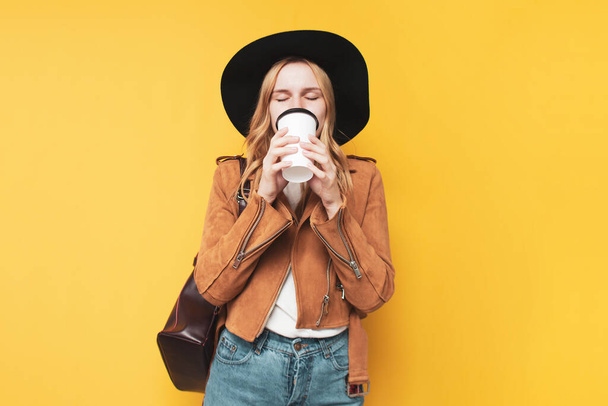 young girl in autumn clothes drinks coffee on a yellow isolated background - Foto, Imagen