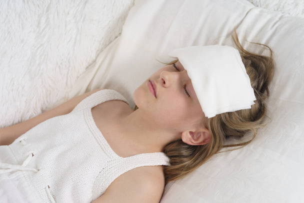 A sick teenage girl lies on her head with a wet rag to remove heat. Medical concept. - Фото, изображение