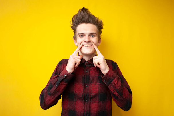 νεαρός θετικός τύπος κάνει τα δάχτυλα χαμόγελο σε κίτρινο απομονωμένο φόντο, ο άνθρωπος σε καλή διάθεση - Φωτογραφία, εικόνα