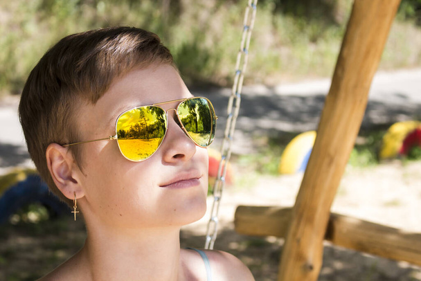 Portret dziewczynki w żółtych okularach przeciwsłonecznych, w której soczewkach odbijają się drzewa - Zdjęcie, obraz