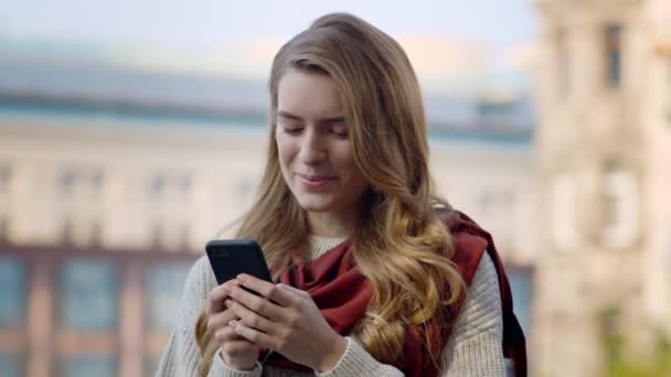 Радостная девушка пользуется телефоном на открытом воздухе. Улыбающаяся женщина стоит с телефоном на улице
. - Кадры, видео