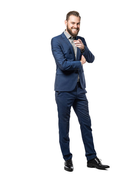 A full body picture of a happy caucasian male smiling and pointing at the camera, wearing ablue suit standing against a white background. - Valokuva, kuva