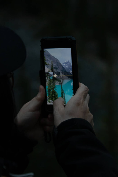 Ktoś robi zdjęcie jeziora Moraine w nocy przy użyciu smartfona. Park Narodowy Banff, AB Kanada - Zdjęcie, obraz