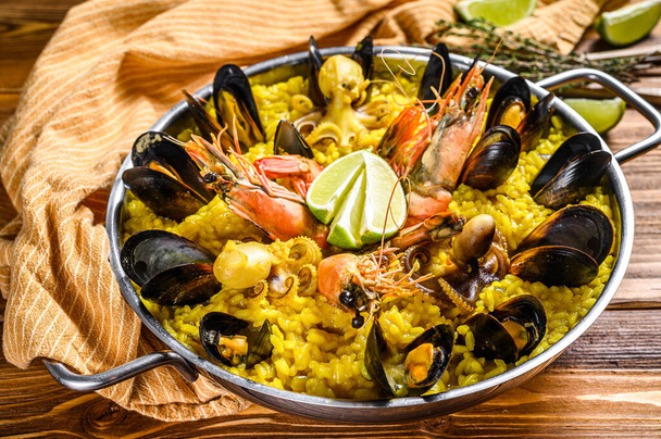 The Spanish paella with seafood prawns, shrimps, mussels in a paellera. Wooden background. Top view. - Photo, Image