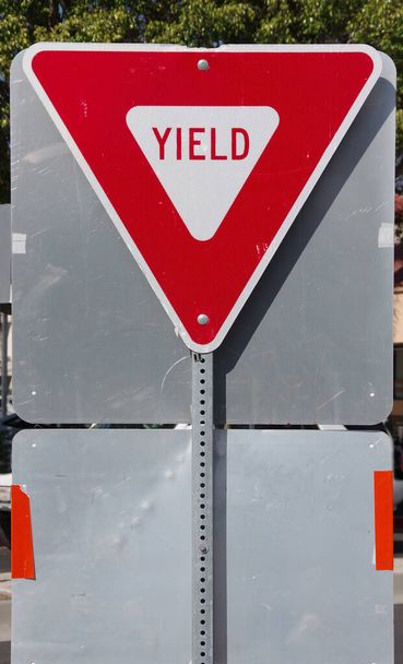 Vista de cerca de un letrero YIELD en una salida de autopista montada en la parte posterior de otras señales de tráfico
 - Foto, imagen