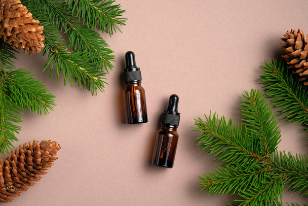 Flat lay composition with bottles of conifer essential oil on beige background with pine tree branches and cones. Natural organic cosmetic for hair care. - Фото, зображення
