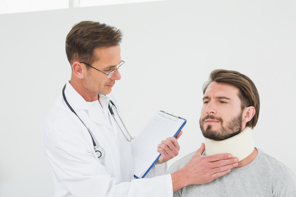 Male doctor examining a patient's sprained neck - Foto, Imagen