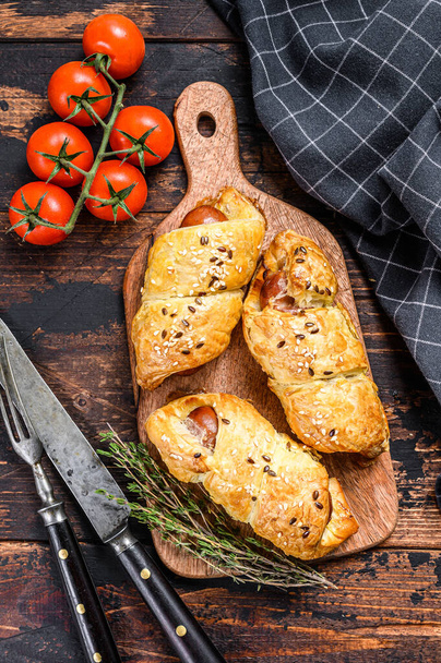 Cutting board with sausage rolls in the dough. Dark wooden background. Top view. - Foto, Imagem