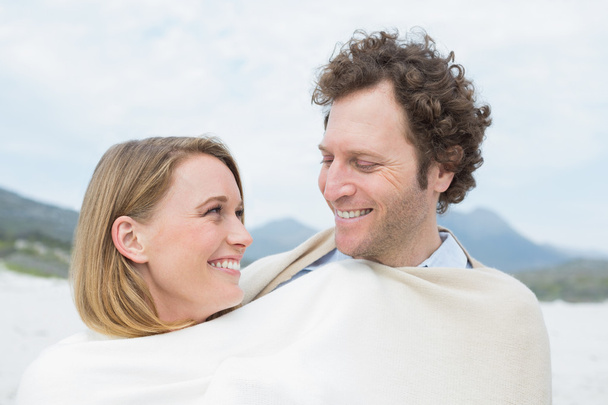 Smiling couple wrapped in blanket at beach - Фото, изображение
