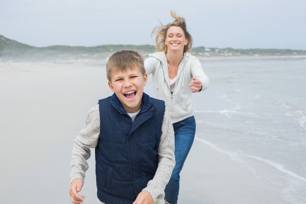 Woman and cheerful boy running at beach - Фото, изображение
