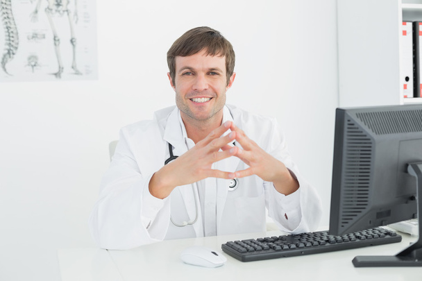 Smiling male doctor with computer at medical office - Foto, imagen