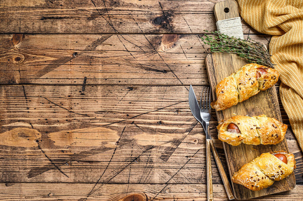 Cutting board with sausage rolls in the dough. wooden background. Top view. Copy space. - Photo, Image