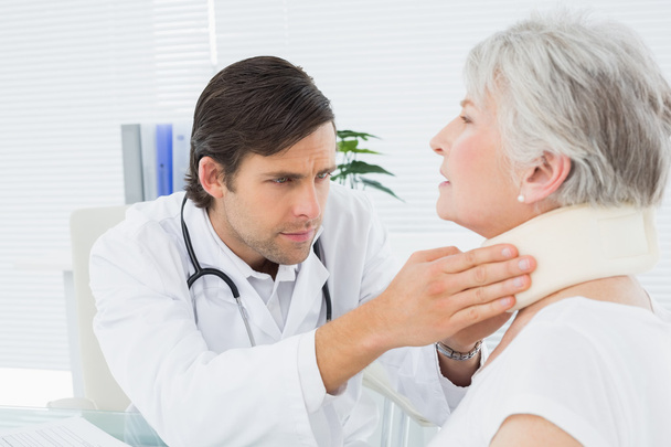 Male doctor examining a senior patient's neck - Foto, afbeelding
