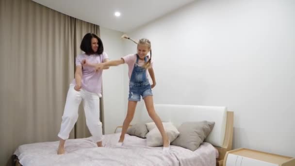 Gelukkig jong moeder en schattig dochtertje dansen, springen op bed, lachen moeder spelen met opgewonden schattige tiener kind in de slaapkamer, grappig familie activiteit thuis, plezier hebben - Video