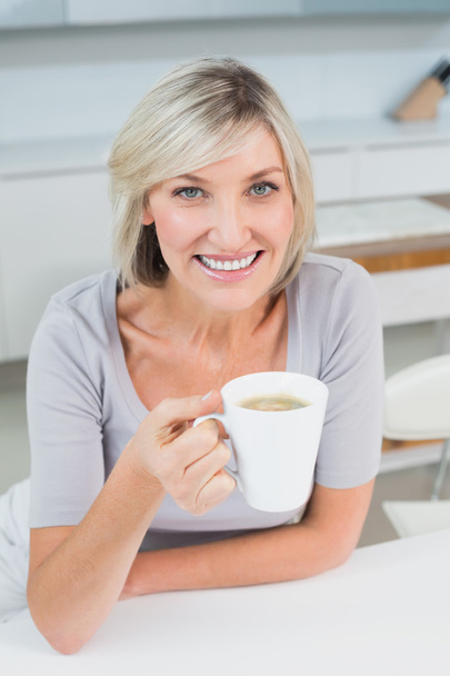 Smiling young woman with coffee cup in kitchen - Fotografie, Obrázek