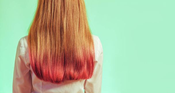 Ένα κορίτσι με μερικώς χρωματιστά μαλλιά σε ροζ σε ανοιχτό πράσινο φόντο. - Φωτογραφία, εικόνα