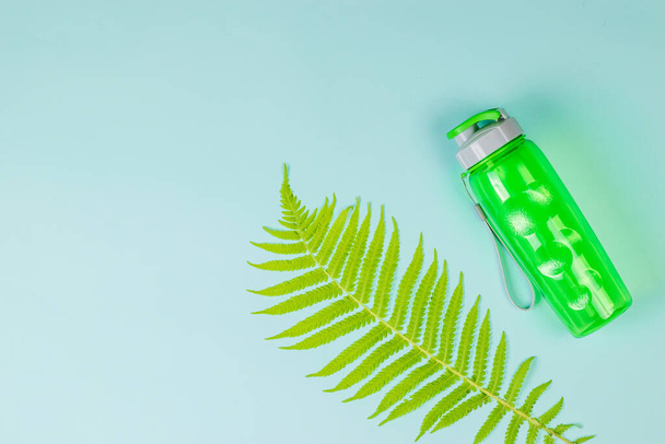 Grüne Sportwasserflasche und Palmblatt auf blauem Hintergrund. Flache Lage. - Foto, Bild